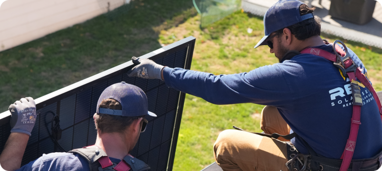 Technicians handling a solar panel during rooftop solar work