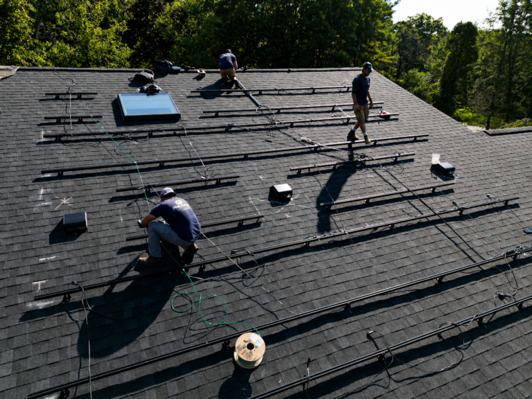 Crew installing solar racking rails on a shingle roof
